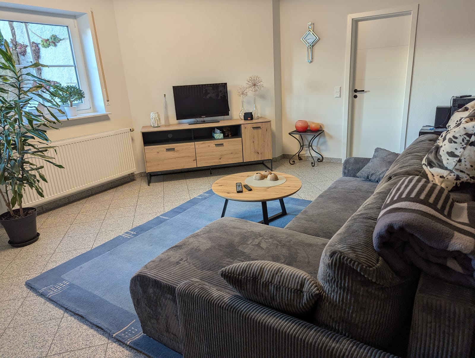 Wohnbereich mit großer Couchgarnitur, Couchtisch, Fernseher und Fenster zum Garten